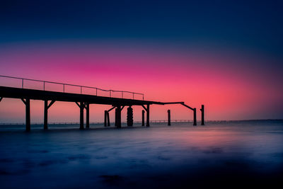 Silhouette bridge over sea against sky during sunset