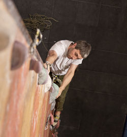 Side view of man with arms raised against wall