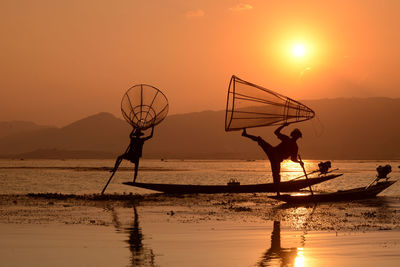 Fishermen fishing in lake against sky during sunset