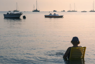 Woman sitting on chair in sea during sunset