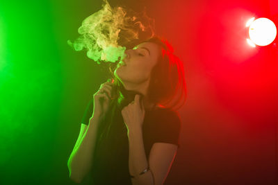 Side view of young woman smoking over black background