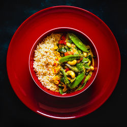 Directly above shot of rice with vegetable in red plate against black background