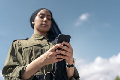 Young woman using mobile phone against sky