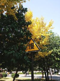 Road sign by trees against sky