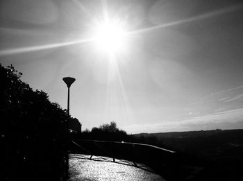 Street amidst silhouette trees against sky on sunny day