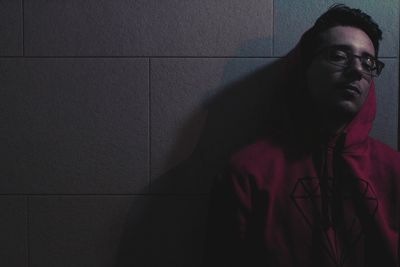 Portrait of man in eyeglasses sitting against wall