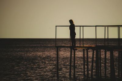 Silhouette woman standing on pier over sea against clear sky