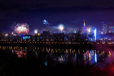 Illuminated city by river against sky at night