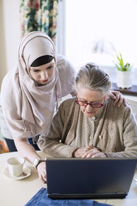 Senior woman with female home caregiver using laptop at table