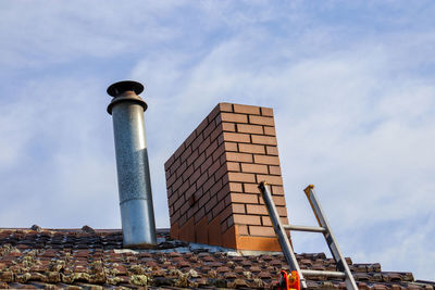 Low angle view of chimney and ladder to roof  against sky