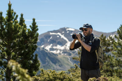 Male hiker photographing through camera while standing on field during sunny day