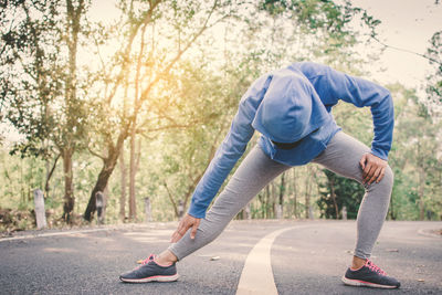 Woman exercising on road amidst trees