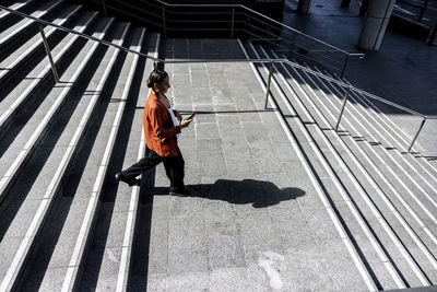 Businesswoman holding mobile phone moving down on staircase