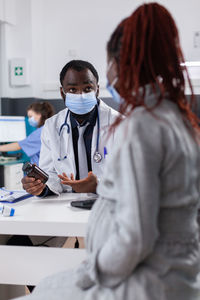 Doctor wearing mask talking with pregnant woman in clinic