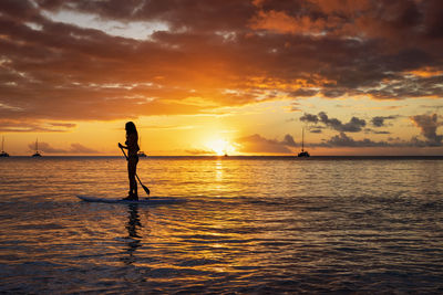 Silhouette woman standing at beach against sky during sunset