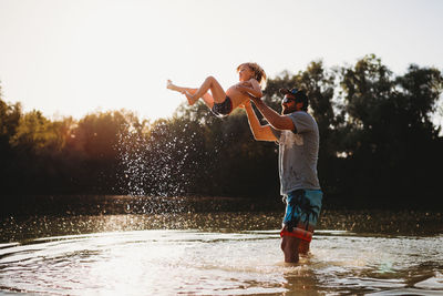 Father holding young child in the air at the lake splashing water