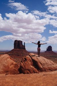 Rear view of woman standing on rock formation against sky