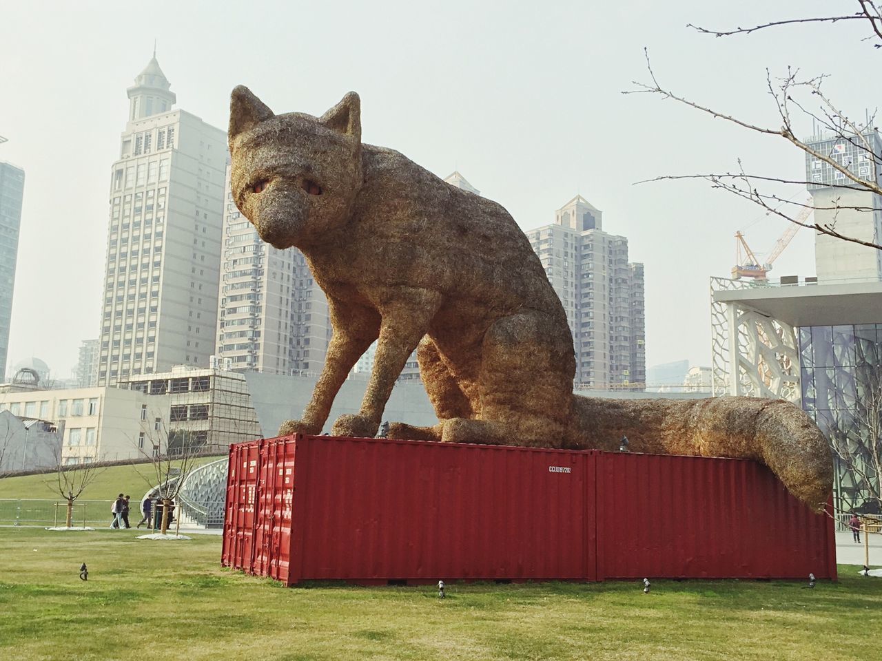 architecture, building exterior, built structure, one animal, clear sky, grass, animal themes, city, tower, domestic animals, tall - high, day, red, skyscraper, tree, sky, outdoors, low angle view, mammal, no people