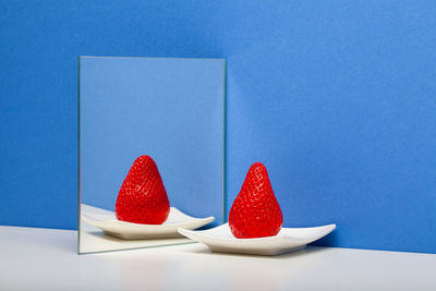 A fresh and tasty strawberry reflected in the mirror on the blue background.