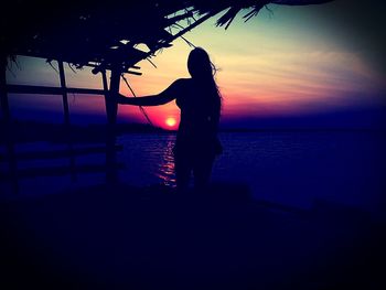 Silhouette woman standing by sea against sky during sunset