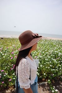 Side view of woman wearing hat standing by plants against clear sky