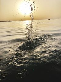 Water splashing in sea against sky at sunset