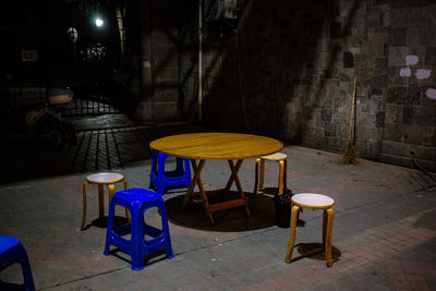 Empty chairs and table against wall at night
