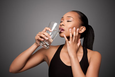 Close-up of young woman drinking water against white background