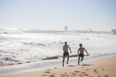 Rear view of men at beach against sky