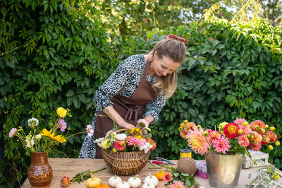 Cute florist girl collects a bouquet of autumn flowers in a basket on the table