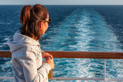 Girl looking at the wake left on the sea by a cruise ship on mediterranean