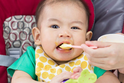 Cropped hand of mother feeding cute son sitting on high chair