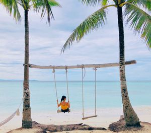 Man sitting on beach by sea against sky