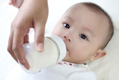 Cropped hand of mother feeding child milk on bed at home