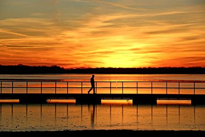Silhouette man standing by railing against orange sky