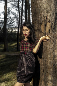 Portrait of young woman standing by tree trunk