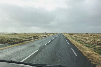 Empty road amidst field leading towards sky