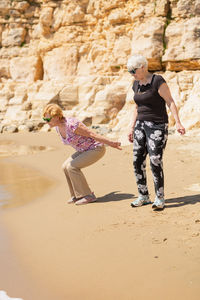 Two senior women walking along the rocky seashore and playing with the waves