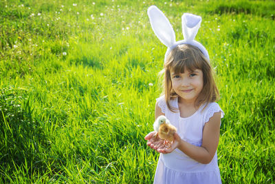 Portrait of young woman with arms raised standing on grassy field