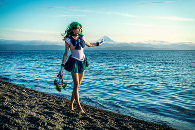 Full length of woman with arms raised standing at beach against sky during sunset