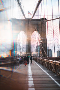 People walking on footbridge in city against sky