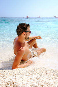 Shirtless man looking away while relaxing at beach