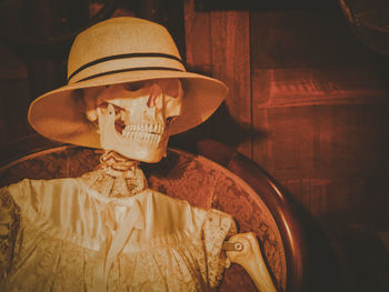 Close-up of human skeleton with hat on chair at home