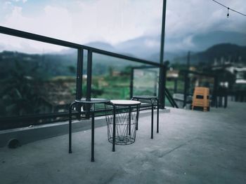 Empty chairs and tables against sky seen through glass window