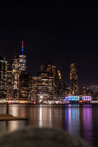 Illuminated buildings by river against sky at night