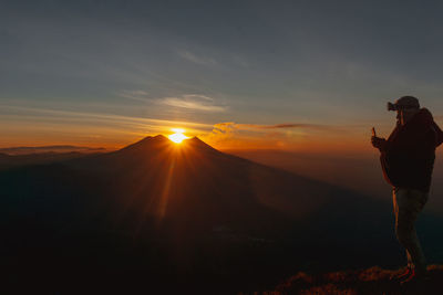 Silhouette man standing on mountain against sky during sunset