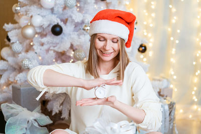 Beautiful woman in santa hat holds an alarm clock and smiles cute against