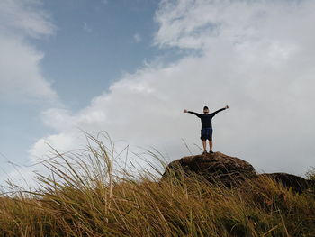 Low angle view of man standing on mountain against cloudy sky