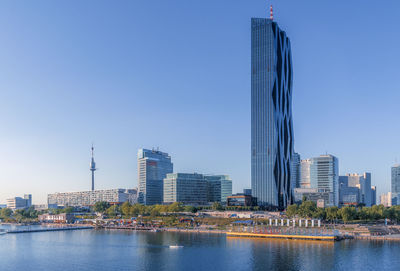 Modern buildings by river against clear sky