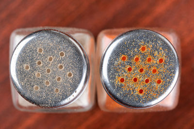 Top view of the lids of two glass pepper pots with black and red ground peppers.
